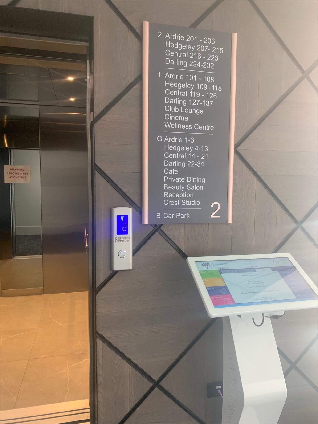 A white Blue Cross touch screen kiosk beside a lift with a directory