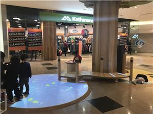Children watching an interactive floor projection around a wooden tree play structure at Chadstone