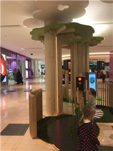 A child at a tree-themed play area with a traffic light and bench in a shopping centre