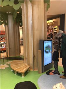 A boy using a touch screen game beside a bench in the Chadstone tree play area