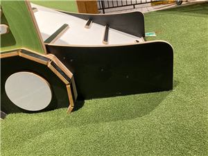 A black and white timber play structure with a ramp on artificial grass at Grand Central Shopping Centre