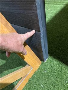 A person pointing to the timber edge of a play structure on artificial grass