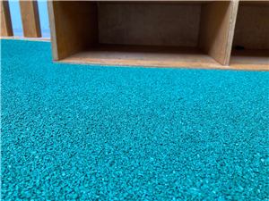A teal rubber play floor beside a timber shelf