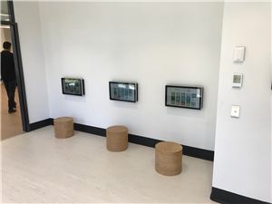 Three wall-mounted touch screens and wooden stools in a bright children's room
