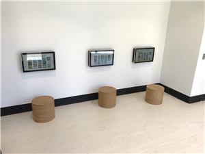Three touch screens and round timber stools along a white wall in a kids room