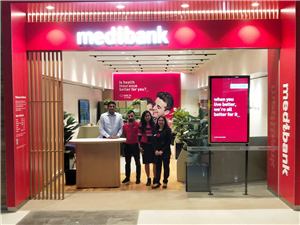 Staff standing at the counter inside a Medibank store with a red entrance sign