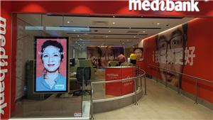 A Medibank store window with a portrait digital screen and red feature wall