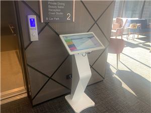 A white Blue Cross touch screen on a stand beside a lift