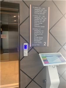 A white touch screen kiosk beside a lift with a directory in an aged care home