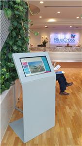 A white touch screen kiosk in an aged care reception with a Blue Cross sign