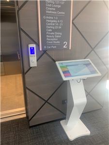 A white touch screen kiosk on a pedestal beside a building directory