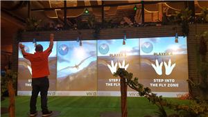 A man reaching up at a four-player dinosaur Fly Zone game wall