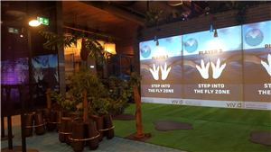 A dinosaur Fly Zone game wall with four player stations and tropical plants
