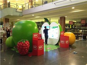 A giant apple with a raspberry, an orange and a family using an interactive screen