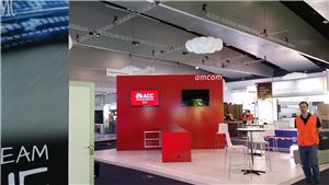 An Amcom exhibition stand with a red wall and screens