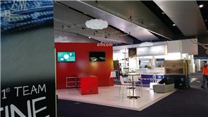 An Amcom exhibition stand with a red wall and tall tables