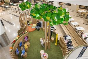 A tree-themed play pod with kids screens beside a food court