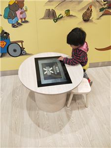 A child using a round touch table in a play room with a mural