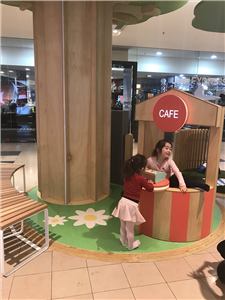 A child at a shop play kiosk beside a tree in a shopping centre