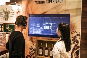 A Jameson airport stand with two people watching an interactive screen