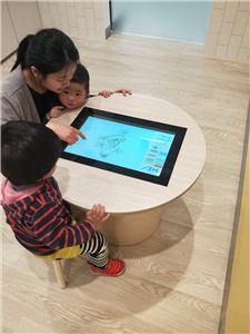 A parent and children using a round touch table in a children's room