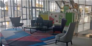 A waiting lounge with armchairs and a coloured rug near a shopping centre entrance