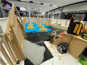 A blue and yellow play floor taking shape inside a timber fence