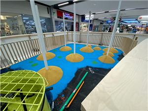 A blue and green play floor with sand mounds being installed in a shopping centre