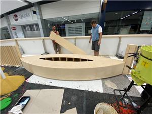 Workers building a boat-shaped timber play piece in a shopping centre