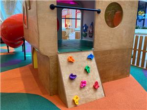 A timber house cubby with a climbing wall and red tube slide at Grand Central Shopping Centre