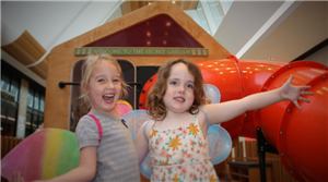 Two smiling girls in front of the Secret Garden house and red slide