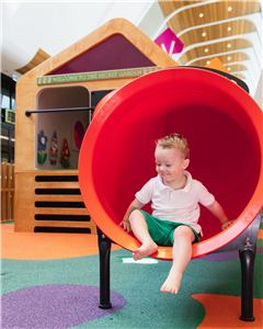 A toddler sitting in the red tube slide at Grand Central