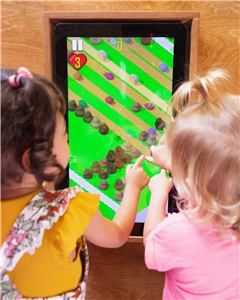 Two toddlers playing a touch screen game built into the play wall