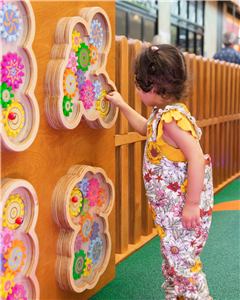 A girl playing with a flower gear panel on the timber play wall
